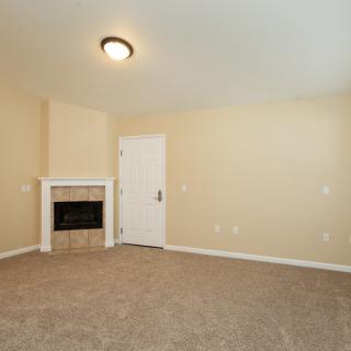An empty room with beige walls, a carpeted floor, and a small fireplace next to a door.