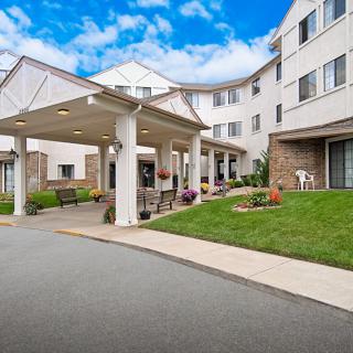 The image shows the entrance of a residential building with a driveway and landscaped surroundings.