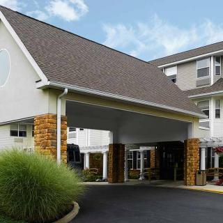 The image shows the entrance of a hotel with a modern design and landscaped surroundings.