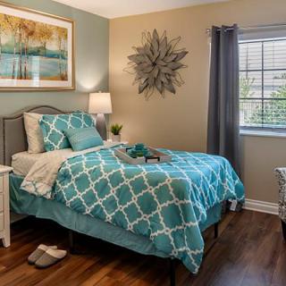 A cozy modern bedroom featuring teal bedding, elegant wall art, and wooden flooring.