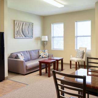 A cozy living room featuring a sofa, coffee table, dining set, and decor elements like a lamp and wall art.