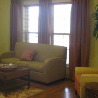 A cozy living room with a sofa, armchair, and coffee table in front of large windows with curtains.