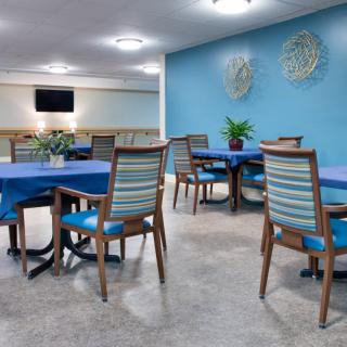 A dining room with blue-accented decor, featuring striped chairs and tables set against a bright wall.