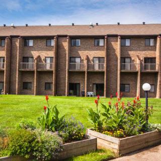 A brick residential building with balconies overlooking a well-maintained lawn and garden.
