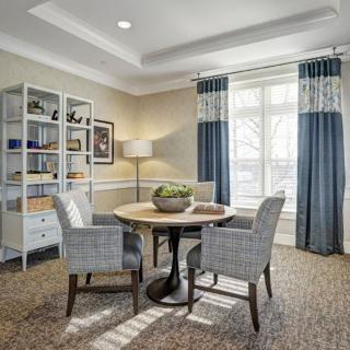 A cozy living room with a round table, chairs, and a bookshelf near the window.