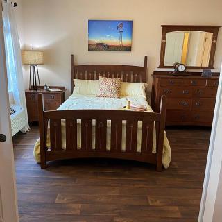 A cozy bedroom featuring a wooden bed, dresser with mirror, and a floor lamp on wood flooring.