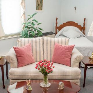 A cozy living space with a striped sofa and pink pillows, adjacent to a bed, featuring floral decor.