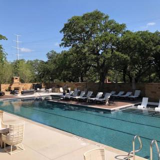 A serene outdoor swimming pool surrounded by trees and lounge chairs under a clear blue sky.