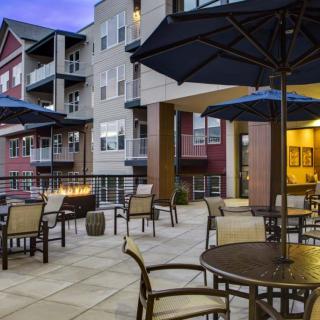 An inviting outdoor patio at an apartment complex, featuring tables and chairs under large umbrellas with a cozy fire pit.