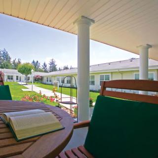 A peaceful outdoor patio area with a wooden table and chairs, featuring a book and overlooking a garden and buildings in the background.