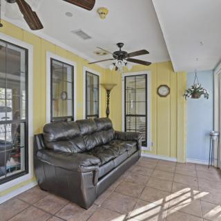 A bright sunroom featuring a leather sofa, ceiling fans, large windows, and indoor plants against yellow walls and a tiled floor.