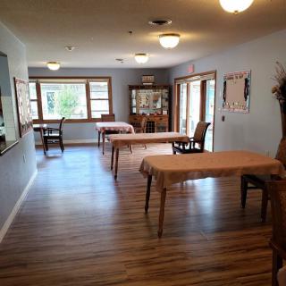 A cozy dining room with wooden floors and several tables set near large windows.