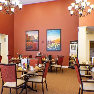 A cozy dining area featuring elegant chandeliers, warm red walls adorned with artistic paintings, and neatly arranged tables and chairs.