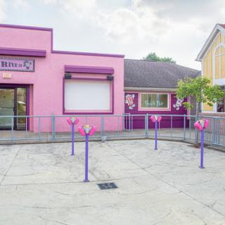 A vibrant pink and purple storefront in an urban setting, featuring a blank sign and decorative elements.