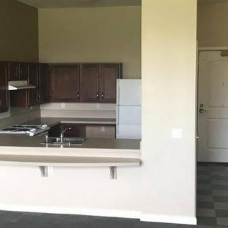 A view of an apartment kitchen with a counter, sink, cabinets, and a refrigerator.