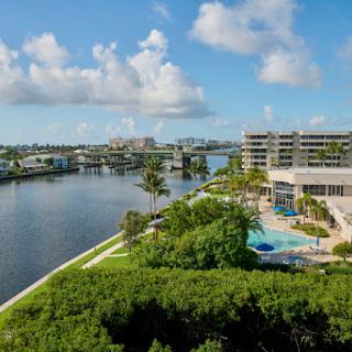 A serene waterfront view featuring a resort-style pool and lush greenery under a sunny sky.