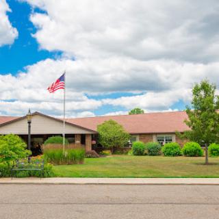 A well-maintained residential building with greenery and an American flag under a partly cloudy sky.