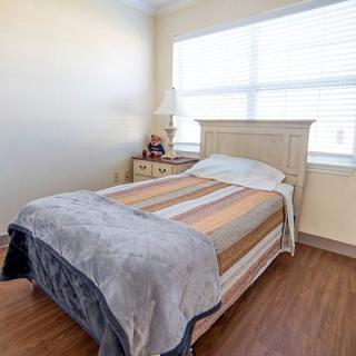 A cozy bedroom with a neatly made bed, a nightstand, and a large window.