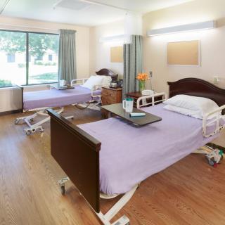 A clean and well-lit hospital room with two adjustable beds and a large window.