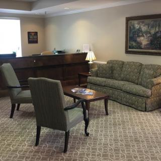 A cozy waiting room featuring a sofa, chairs, and a wooden desk with a lamp.