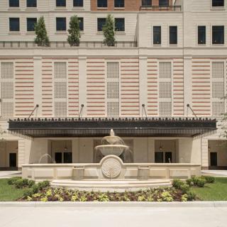 A view of an elegant building facade with a central fountain and landscaped surroundings.