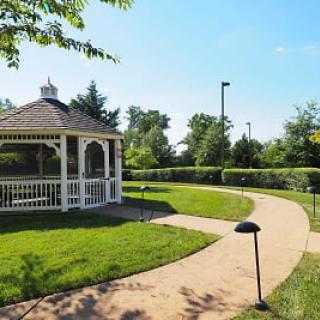 A serene garden featuring a charming gazebo and a winding pathway, surrounded by lush greenery under a clear blue sky.