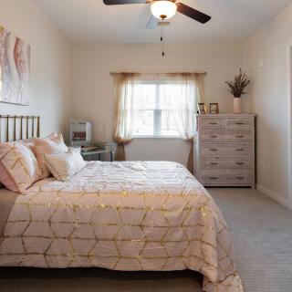 A cozy bedroom with a double bed, a dresser, and a ceiling fan.