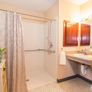 A bathroom with a shower area, sink, and large mirror under warm lighting.