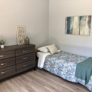A minimalist bedroom with a single bed and dresser, featuring modern decor and wood flooring.
