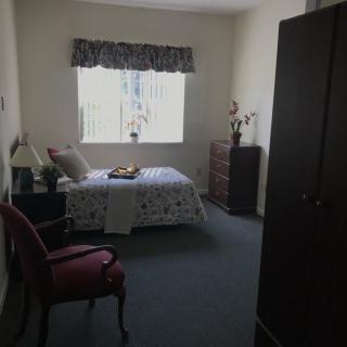 A cozy bedroom with a bed, chair, and wardrobe near a window.