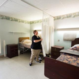 A nurse adjusts the privacy curtain in a patient room within a healthcare facility.