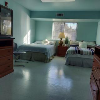 A spacious bedroom featuring two twin beds, dressers, and a lamp by the window.