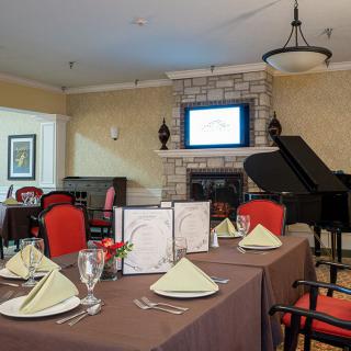 An elegant dining area with neatly arranged tables and chairs, featuring a grand piano and a fireplace.