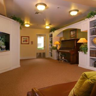 A cozy living room with a piano and bookshelves, warmly lit by ceiling lights.