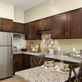 A modern kitchen with dark wooden cabinetry, a granite countertop, and stainless steel appliances.