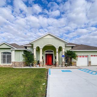A suburban house with a red front door and a spacious driveway under a cloudy sky.