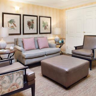 A cozy living room with a sofa, armchairs, and a large coffee table, adorned with artwork and soft lighting.