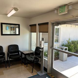 A cozy waiting area featuring chairs, a mirror, and natural light streaming in through the open doorway.