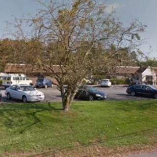 A parking lot with several cars, surrounded by trees and grass on a clear day.