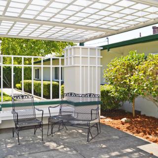 An outdoor patio with metal chairs under a pergola, surrounded by greenery.