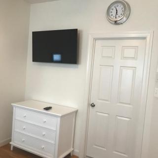 A room with a wall-mounted television, a white dresser, and a door with a clock above it.