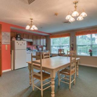 A cozy kitchen and dining area with a wooden table, chairs, and ample natural light from large windows.