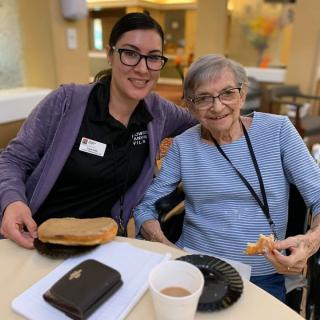 A caregiver and an elderly person enjoying a meal together indoors.