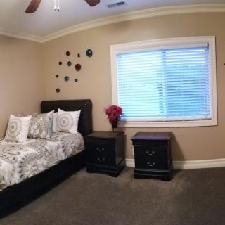 A cozy bedroom with modern decor, featuring a bed and nightstands near a window with blinds.