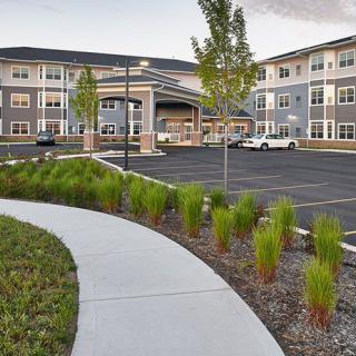 A view of a modern retirement home with neatly landscaped surroundings and a parking area.