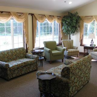 A cozy living room setup featuring floral-patterned sofas and comfortable chairs, illuminated by natural light from large windows.