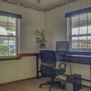 A home office with a desk, computer, and chair near two windows.