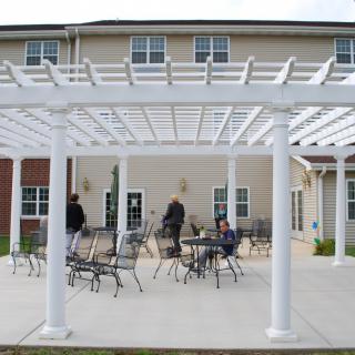 An outdoor patio area featuring a white pergola and metal furniture in front of a building.
