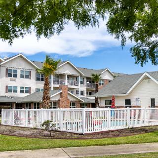 A residential building with a white fence and palm trees under a cloudy sky.