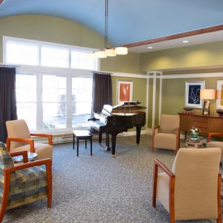 A cozy living room with a grand piano, surrounded by comfortable seating and large windows.